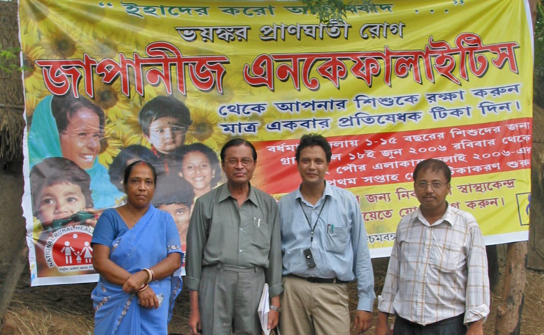 Health center staff with Dr. Mukergee and children standing in front of Japanese Encephalitis poster, West Bengal, India, July 2006