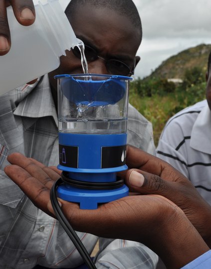 A close-up of water being poured into an MSR SE200 Community Chlorine Maker (electrochlorinator) held in one hand.