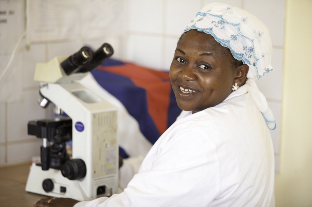 A laboratory technician looks up from a microscope as she works in a lab.