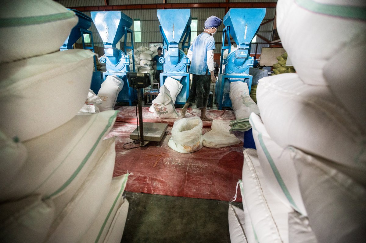Employee supervising machine filling large bags with rice flour, with stacks of the bags in the foreground.