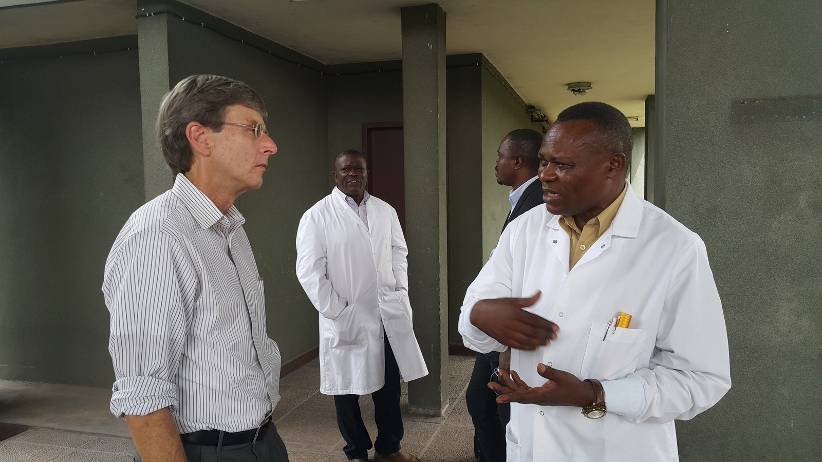 David Fleming talks to a health care worker outside a building as two other men look on. 