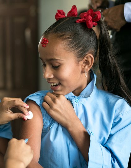 A woman gives a girl an injection as others wait behind her.