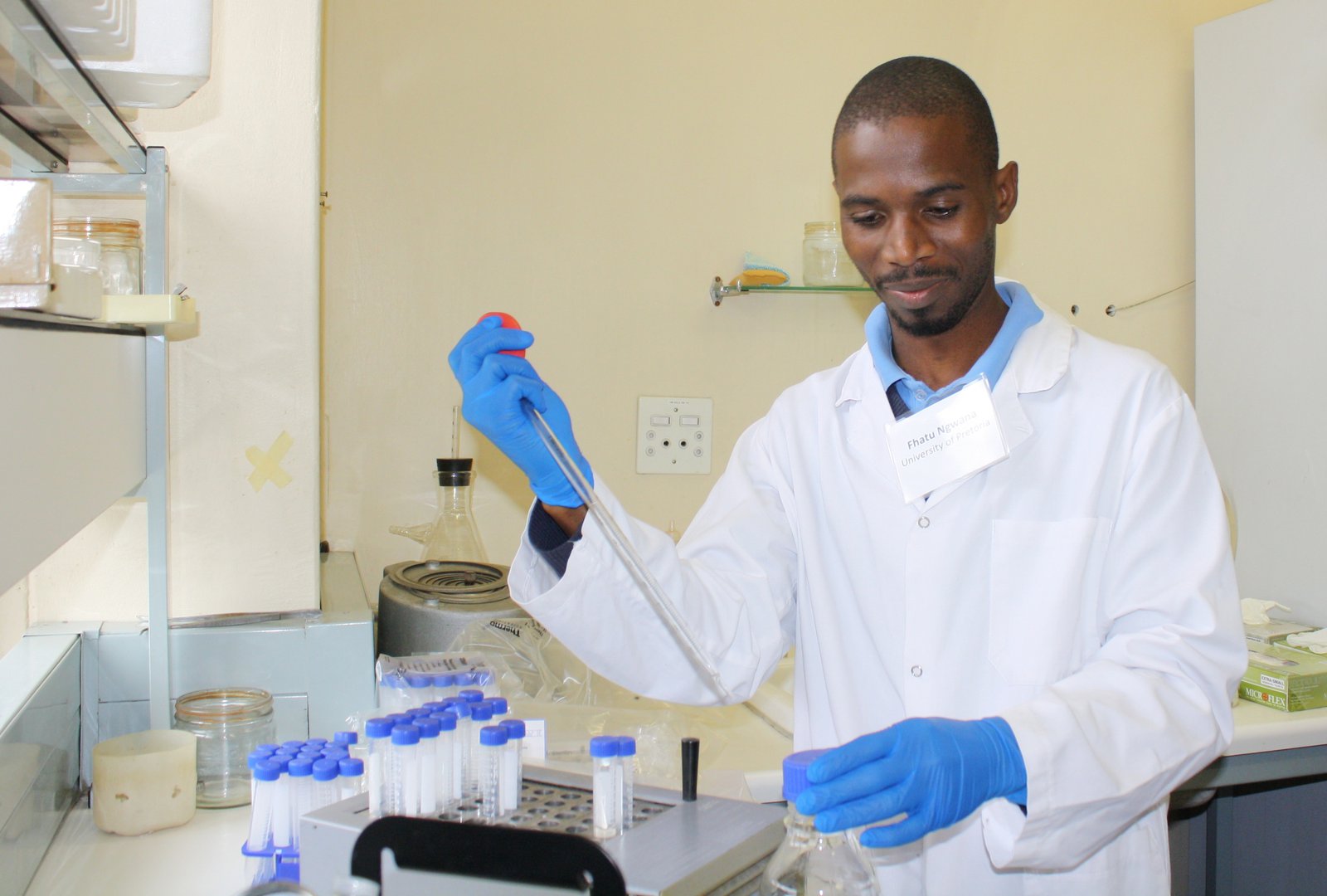 A man in a lab coat holds a test tube.