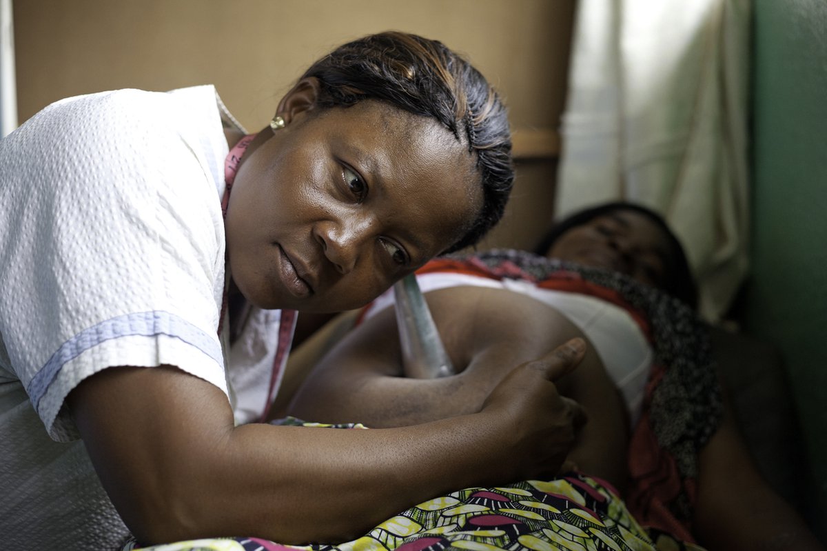 A medical worker listens to a pregnant woman's belly with an ear trumpet.