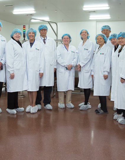 PATH Journeys travelers in China dressed in lab coats and hairnets standing in a semicircle smiling at the camera.