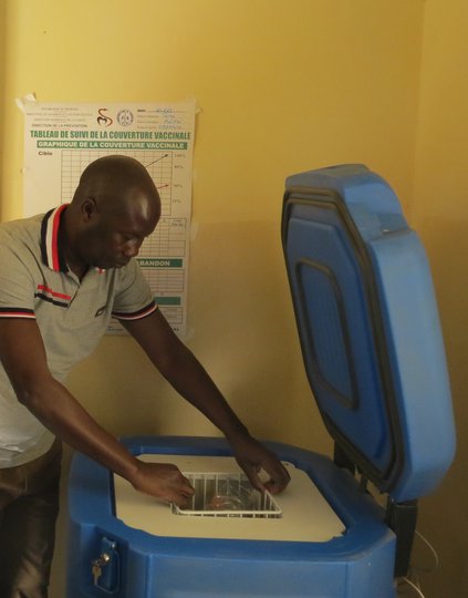 PATH President and CEO Nikolaj Gilbert visits a health center in Mbakhis, Senegal, where Abdoulaye Gueye demonstrates how excess electricity from a solar-powered vaccine refrigerator (shown) helps light the facility at night and charge other devices. Phot