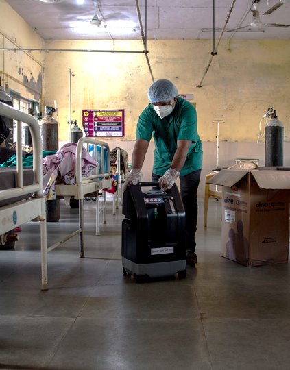 A health care worker unpacks and installs an oxygen concentrator for a COVID-19-positive patient inside an isolation ward at Rural Hospital in Palghar, Maharashtra, India. Photo: PATH/Ragul Krishnan.