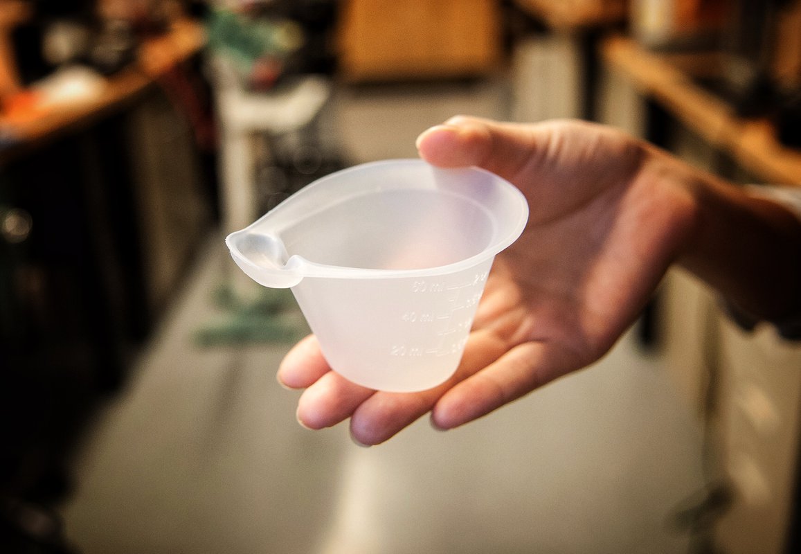 Hand holding the NIFTY cup, a flexible 60 ml cup with a small reservoir extending off the cup lip.