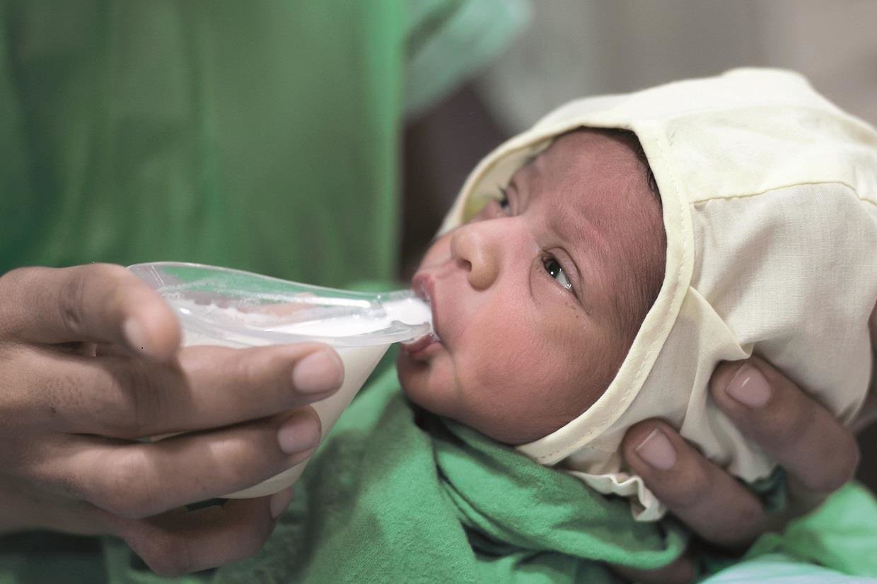 An infant sips human milk from the Nifty Feeding Cup.