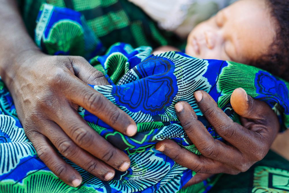 A newborn is wrapped in a blanket and held in two hands.