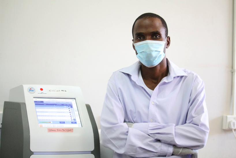 Dr. Ngonda Saasa, UNZAVET lead researcher, stands next to a PCR machine used to diagnose SARS-CoV-2 infections. Photo: PATH/Mirriam Chimba.